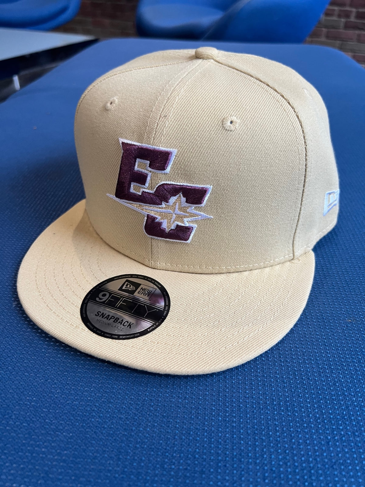 The New Era Baseball Cap, Athletic EC Logo, features beige fabric with maroon and white EC letters and a star embroidered on the front. The 9Fifty sticker is visible on the brim. Offered in three sizes for a perfect fit.