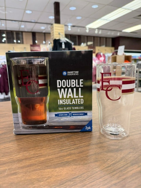 A box of Glass Tumbler 16oz 2pk sits on a table. Beside it, a clear tumbler with red EC letters and stripes is showcased in a retail store setting.