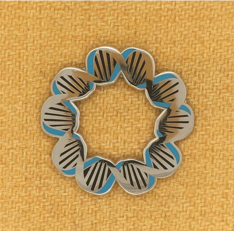 The Rosalind Franklin DNA Pin features a silver and blue double helix in a circular design, elegantly displayed on mustard yellow fabric—a tribute from the Women in Science Collection.