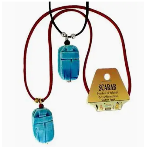 Two blue hand-carved Scarab Necklaces on black and red cords. Tag reads: SCARAB Necklace—symbol of rebirth & transformation. Made in Egypt. Wear as a good luck charm and connect to ancient traditions.
