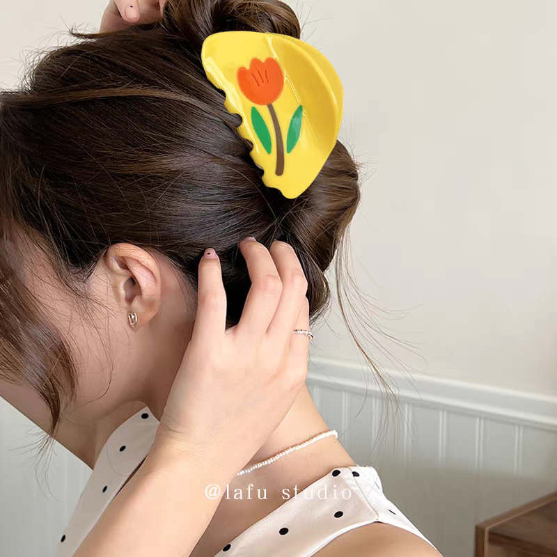 A yellow Tulip Hair Claw Clip holding a woman’s bun in place.