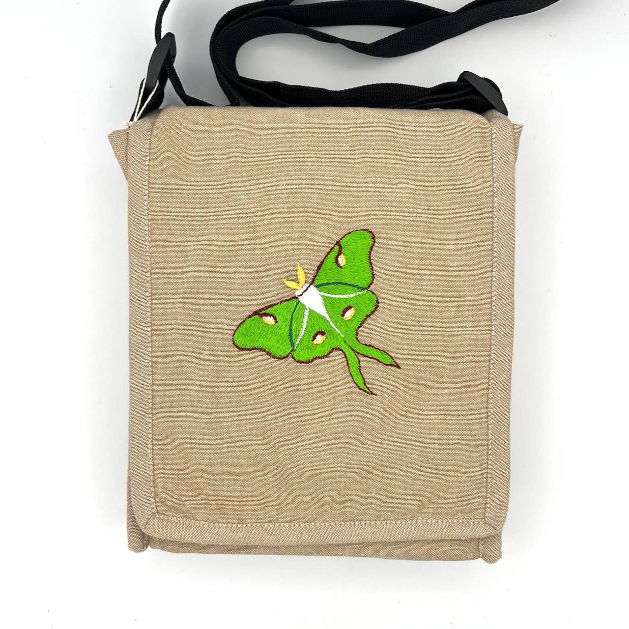 The Luna Moth Field Bag is a beige handmade cotton bag with a green luna moth embroidered on the front flap, black straps, and set against a plain white background.