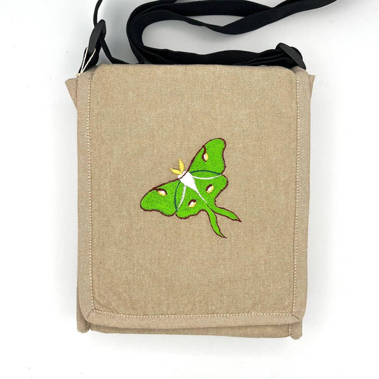 The Luna Moth Field Bag is a beige handmade cotton bag with a green luna moth embroidered on the front flap, black straps, and set against a plain white background.