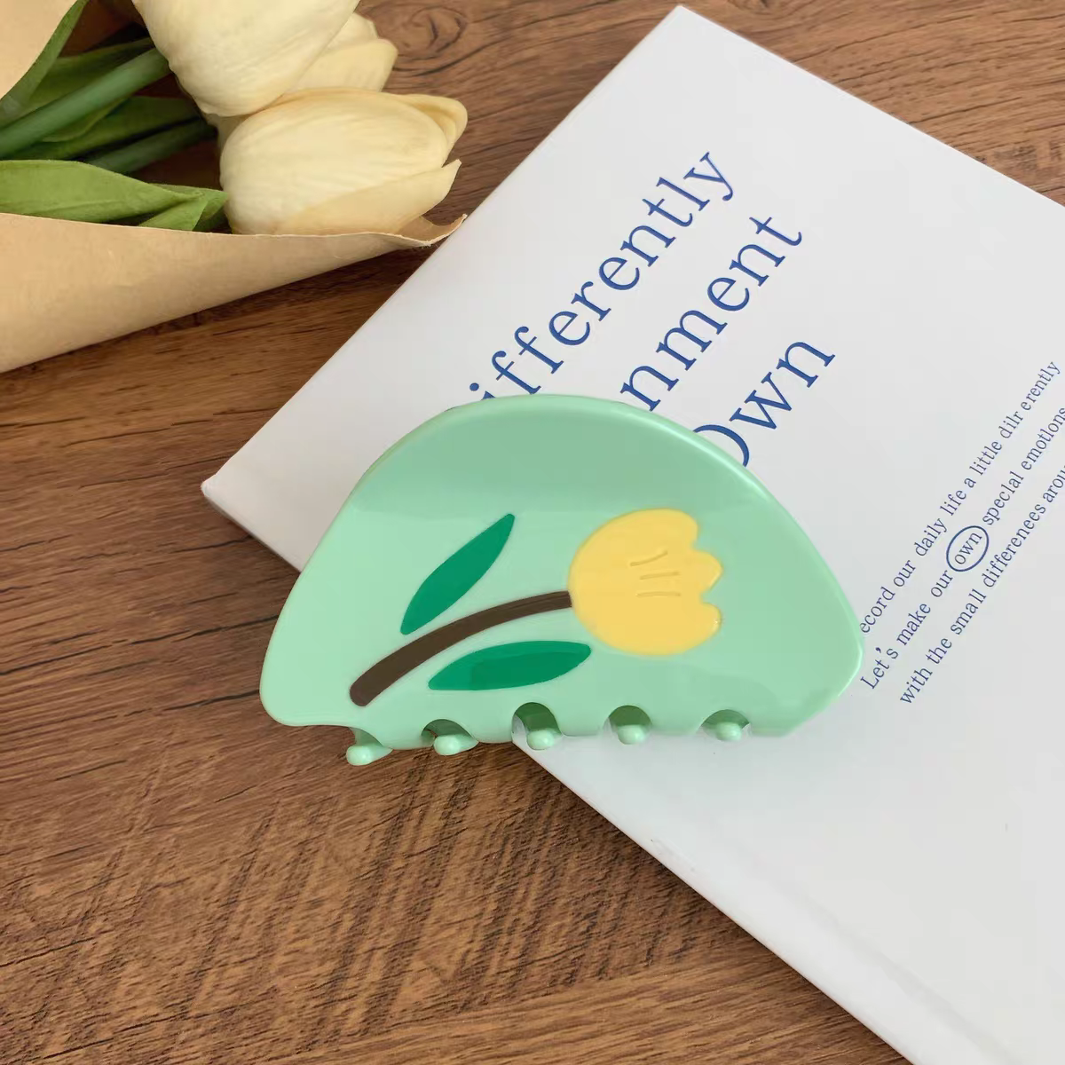 Light green Tulip Hair Claw Clip resting on a closed white book next to a bouquet of tulips.