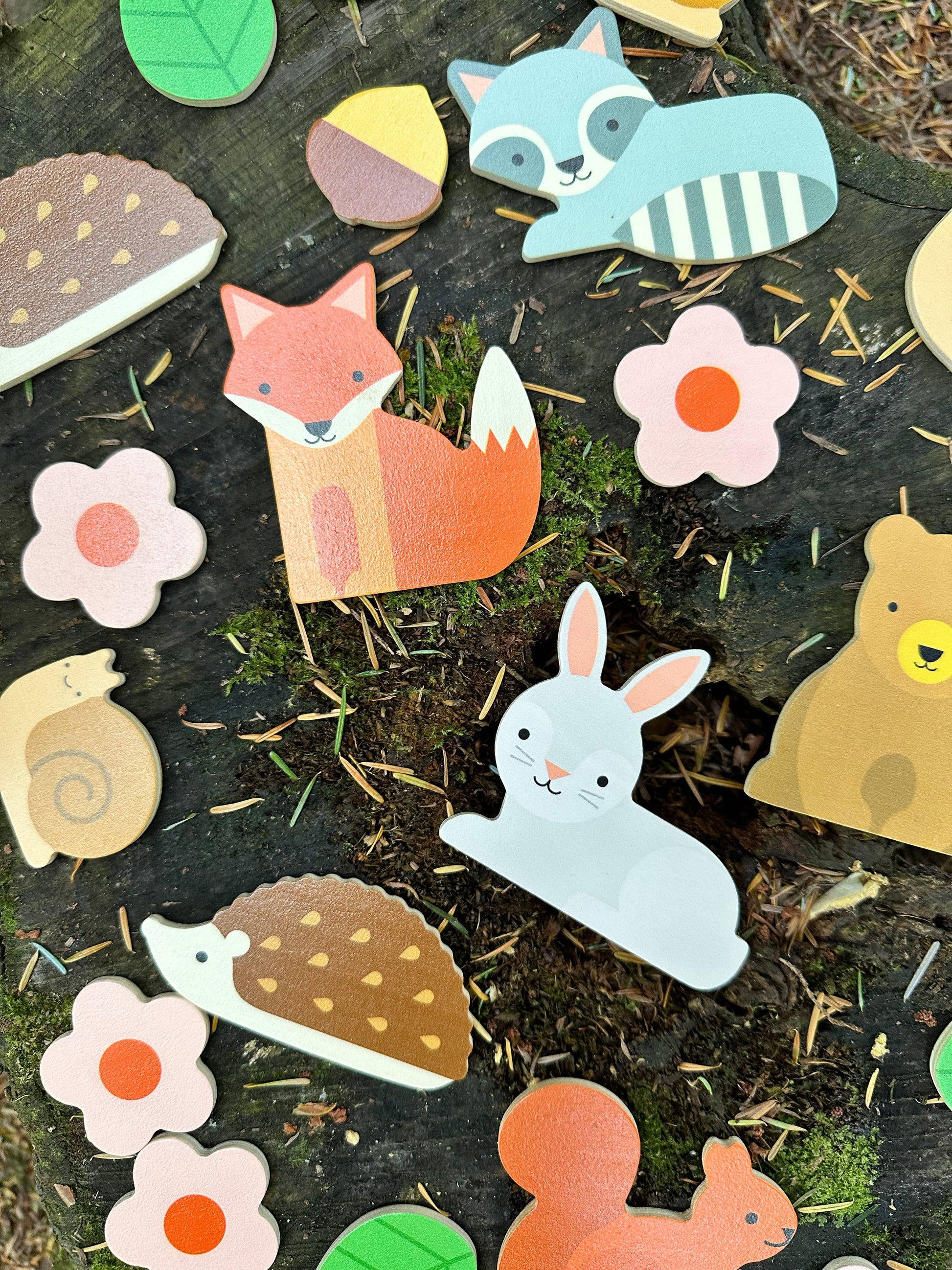 Woodland Wobble: A Wildlife Stacking Game features colorful wooden animal and flower shapes, like a fox, rabbit, and bear, arranged on a tree stump to develop fine motor skills in a fun outdoor setting.