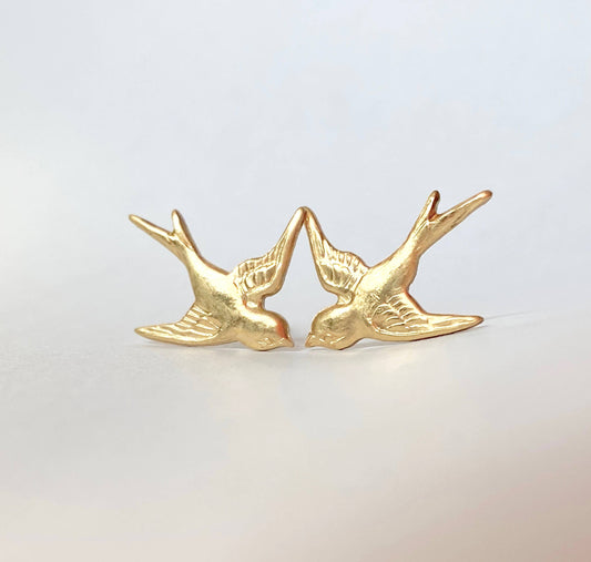A pair of *Flying Sparrow Earrings* in golden brass, beautifully nature-inspired, face each other on a plain, light background—perfect woodland wedding earrings for those who adore delicate details.