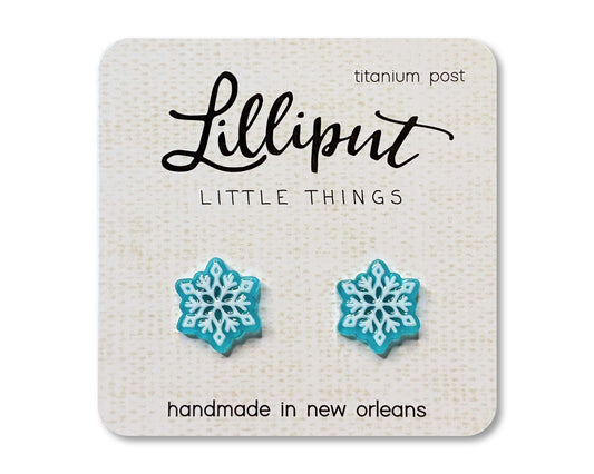 Snowflake Earrings—blue and white snowflake-shaped studs on a card labeled Lilliput Little Things, feature hypoallergenic titanium posts. Handmade in New Orleans, these novelty earrings are as charming as they are comfortable, making them perfect for sensitive ears.