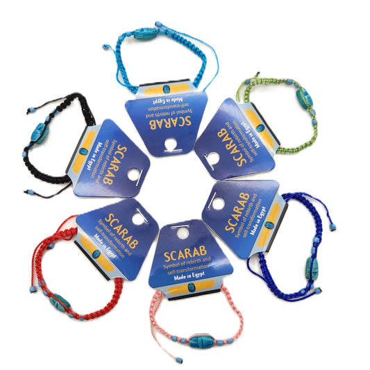 Eight vibrant Macrame Scarab Bracelets, each featuring a blue tag, are arranged in a circle on a white background. The tag describes the soapstone scarab as a symbol of rebirth and notes that it is made in Egypt, emphasizing its tradition as an Egyptian good luck charm.
