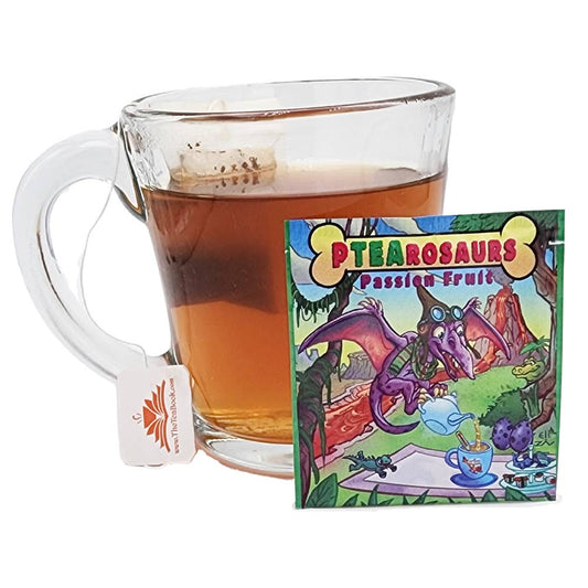 A glass mug of PTEAsaurus passion fruit tea with a tea bag, next to its tea packet featuring a cartoon pterodactyl in a jungle setting.