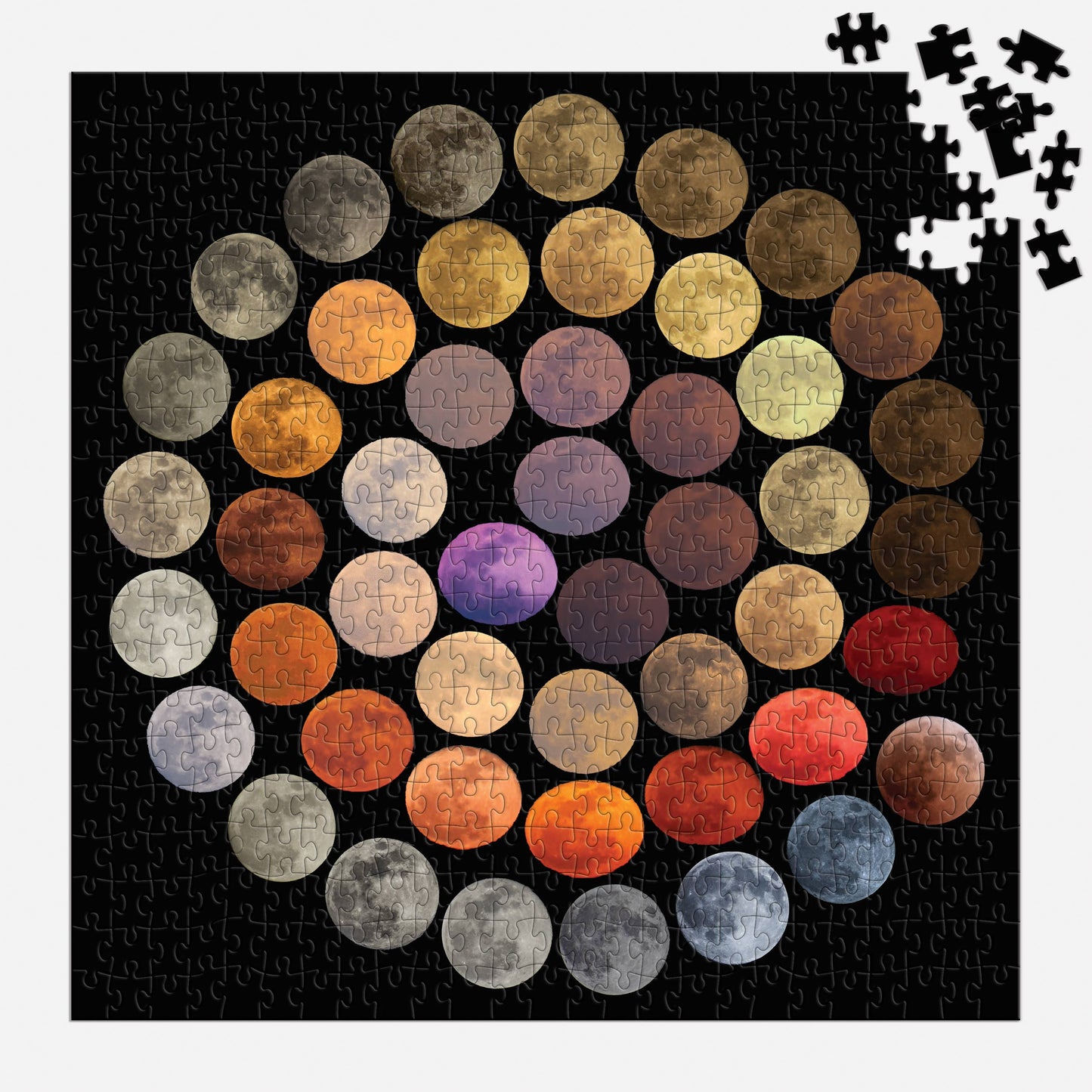 A partially completed Colors of the Moon 500 Piece Puzzle displays colorful moon phases on a black background, with several pieces missing in the upper right and some loose puzzle pieces scattered nearby.