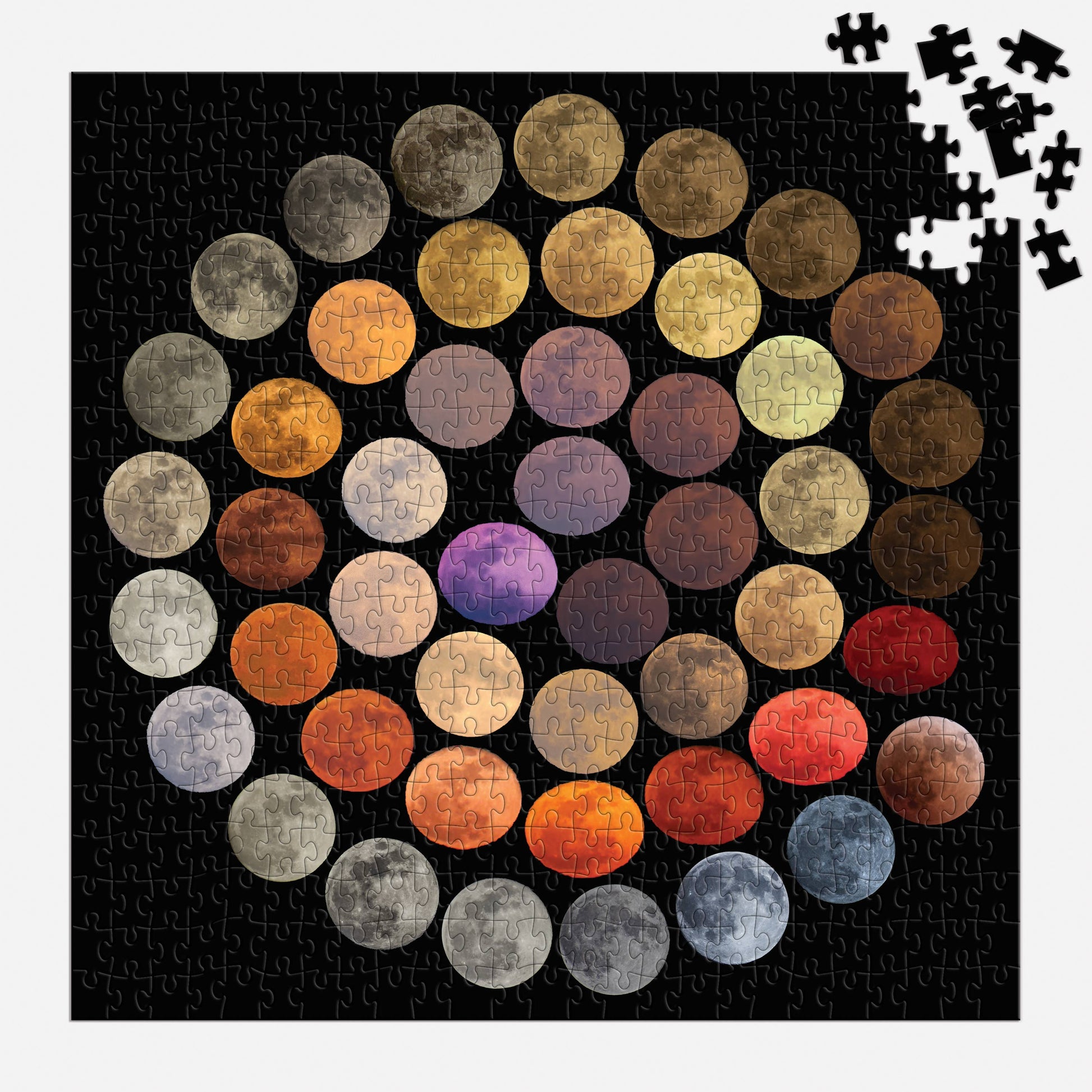 A partially completed Colors of the Moon 500 Piece Puzzle displays colorful moon phases on a black background, with several pieces missing in the upper right and some loose puzzle pieces scattered nearby.