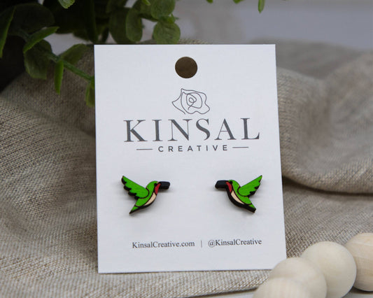Hummingbird Wood Stud Earrings displayed on a white Kinsal Creative card, set against plants and neutral fabric—perfect for handmade jewelry lovers.