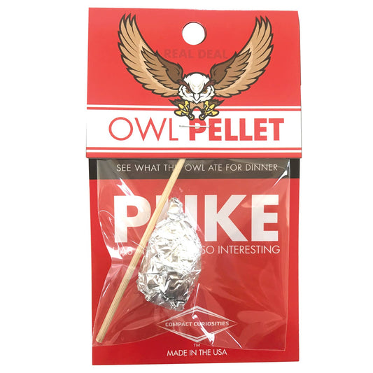 A red package labeled OWL PELLET with an eagle illustration contains a foil-wrapped item and a wooden stick—an exciting science toy to discover skeletal remains. Text includes Real Deal, See what the owl ate for dinner, and Made in the USA.