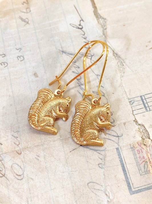 The Woodland Forest Squirrel Earrings rest on vintage paper adorned with handwritten notes and faded markings, capturing the whimsical charm of woodland jewelry inspired by forest creatures.