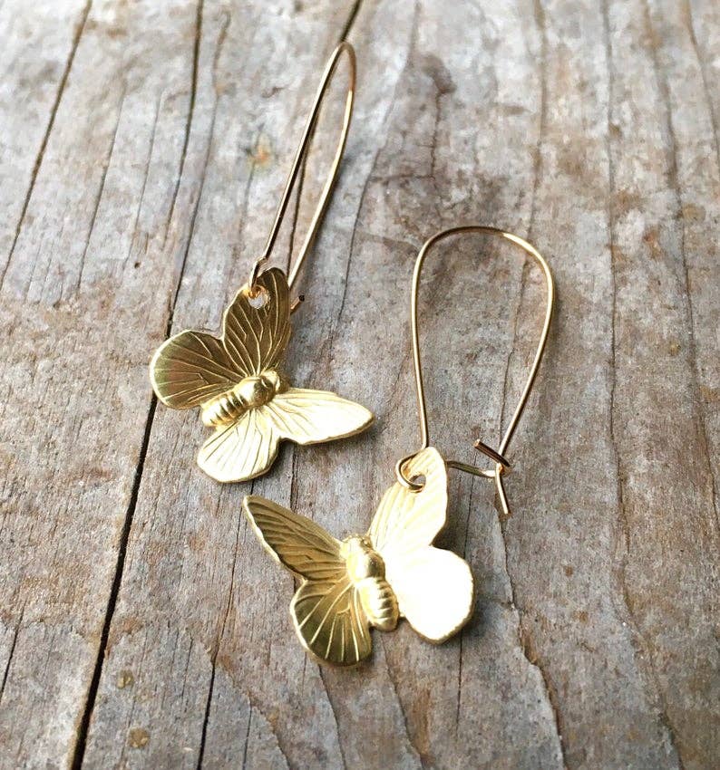 Two SmallButterfly Earrings, crafted in gold and featuring delicate wire hooks, rest on a weathered wooden surface, capturing the whimsical beauty of nature-inspired jewelry.