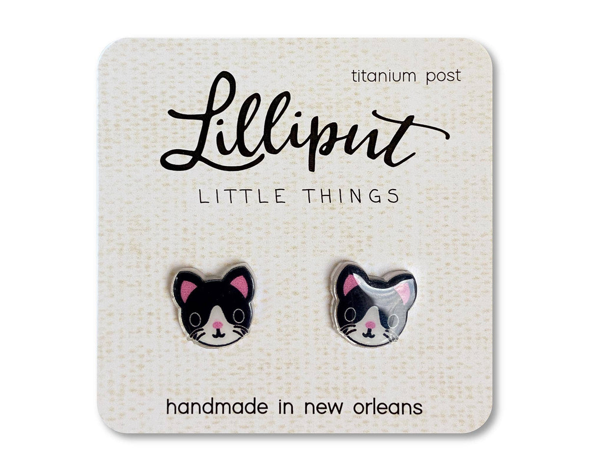Square card displaying two black-and-white Kitty Cat Earrings with pink ears, labeled Lilliput Little Things, featuring titanium posts for hypoallergenic comfort and handmade in New Orleans. The card has a textured beige background.