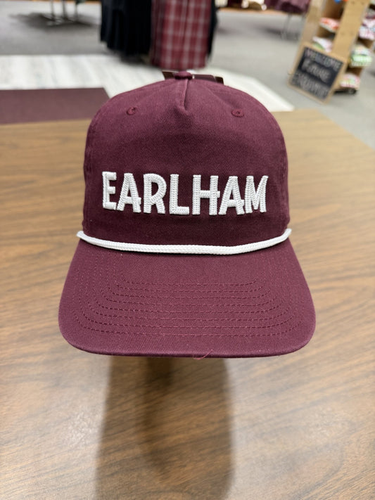 An Earlham Rope Hat in maroon, featuring “EARLHAM” embroidered in large white letters on the front, is displayed on a wooden table indoors.