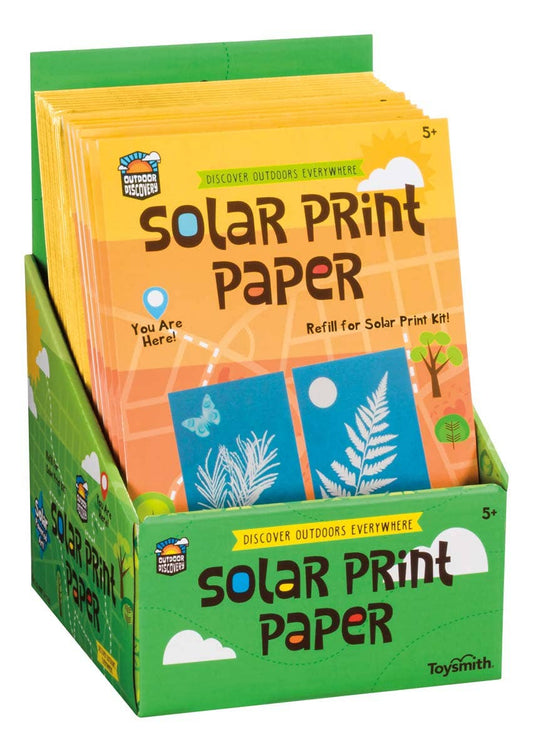 A display box features Outdoor Discovery Solar Print Paper packs in yellow and orange packaging, showing white plant silhouettes on blue backgrounds. Includes sun-sensitive 5" x 7" sheets, ideal for science crafts for ages 5 and up.