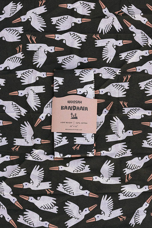 The Migration Bandana is a black cotton bandana with a sublimated white bird print and a beige center label reading WOOSAH BANDANA, LIGHT WEIGHT, 100% COTTON—an iconic piece from Woosah Bandanas.